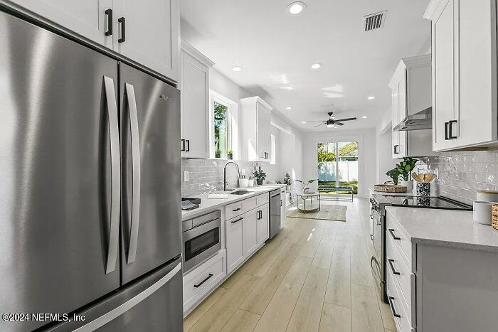 Modern kitchen in small Florida house with white cabinets, stainless steel appliances, and wood flooring.