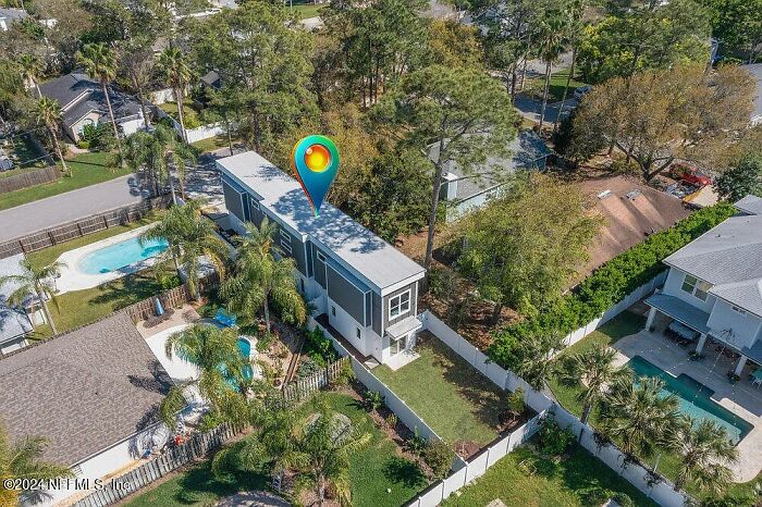 Aerial view of a small modern house in a Florida neighborhood with a nearby pool and trees.