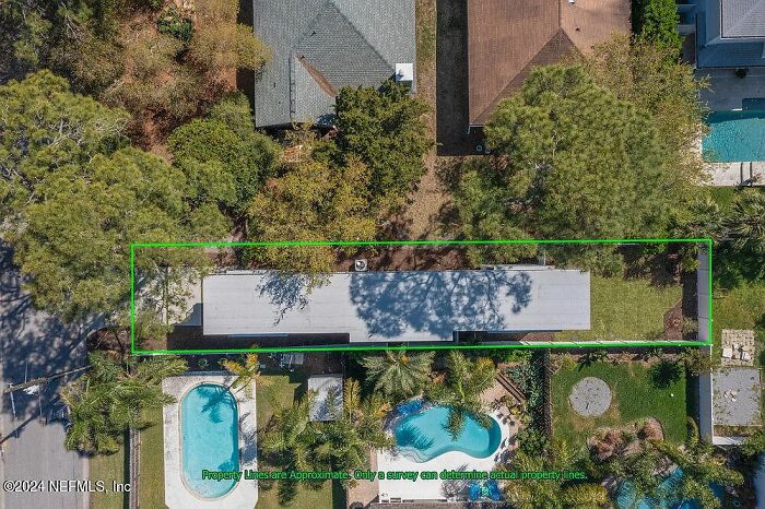 Aerial view of a small house in Florida with neighboring properties and a pool, surrounded by trees.