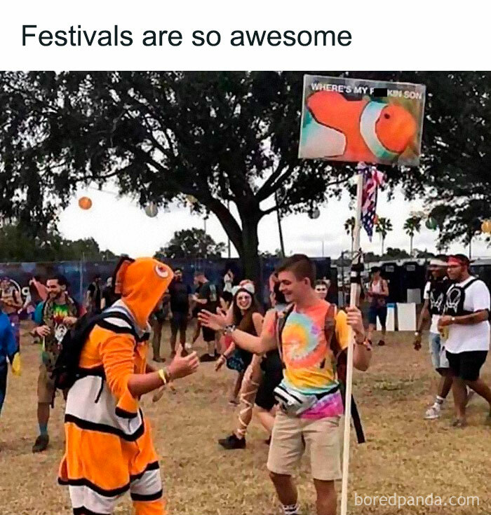 People enjoying a festival, one in a fish costume, holding a funny meme sign; creating random hilarious moments.