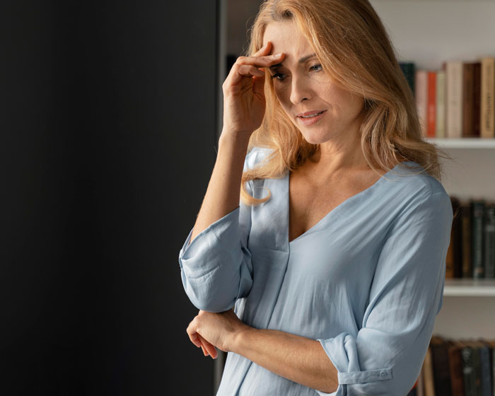 Woman in a thoughtful pose, wearing a blue blouse, standing in a room with bookshelves, pondering family responsibilities.