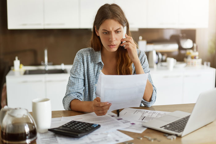 Woman reviewing bills in kitchen, considering action against husband's family.