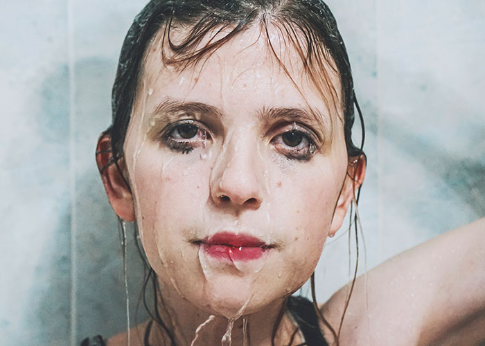 Overwhelmed new mom with wet hair and water on her face, looking directly at the camera.