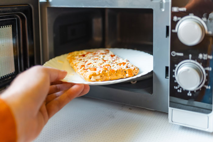 A person placing pizza in a microwave, possibly dealing with cooking drama.