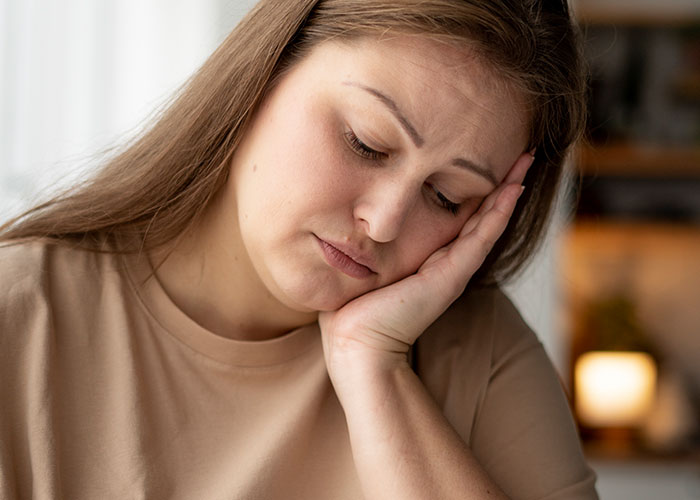 A tired woman rests her head on her hand, seeming exhausted from lack of sleep due to her boyfriend's loud snoring.