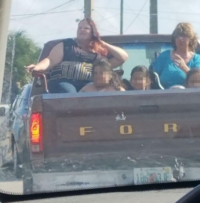 People riding unsafely in the back of a moving pickup truck, illustrating risky behavior on the road.