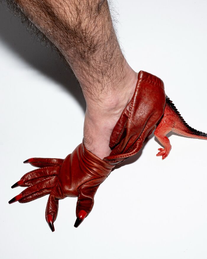 A sculptural footwear piece resembling a dinosaur claw and tail, crafted from red leather, worn on an ankle.