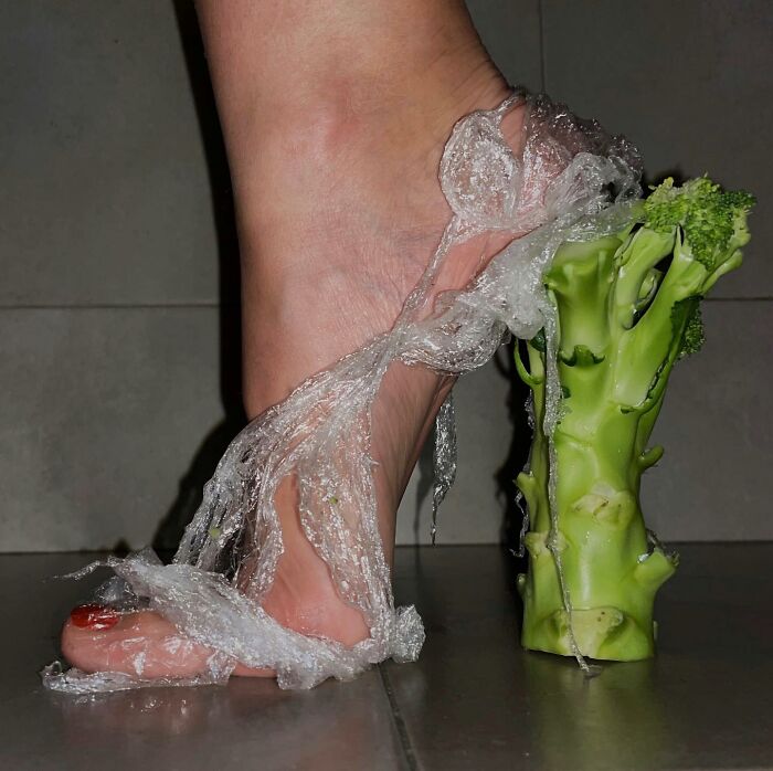 Foot wearing sculptural footwear made from a broccoli stem and plastic wrap, creatively transforming everyday objects.