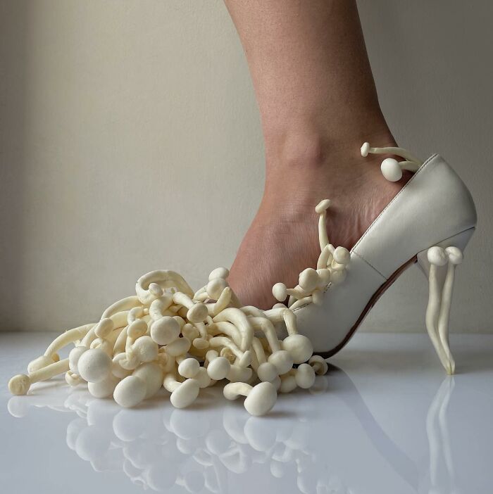 Artistic sculptural footwear with white mushrooms embellishing a high heel shoe.