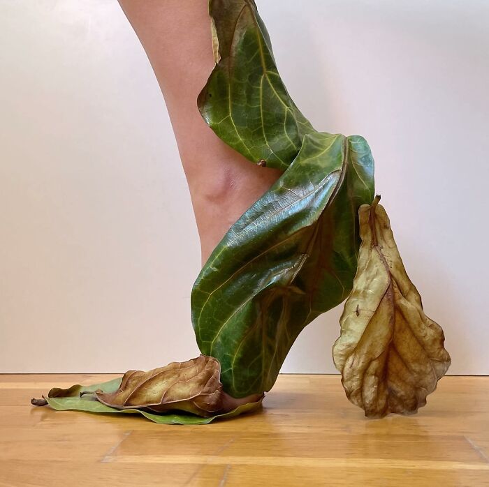 Sculptural footwear made from large green leaves wrapped around a bare foot.