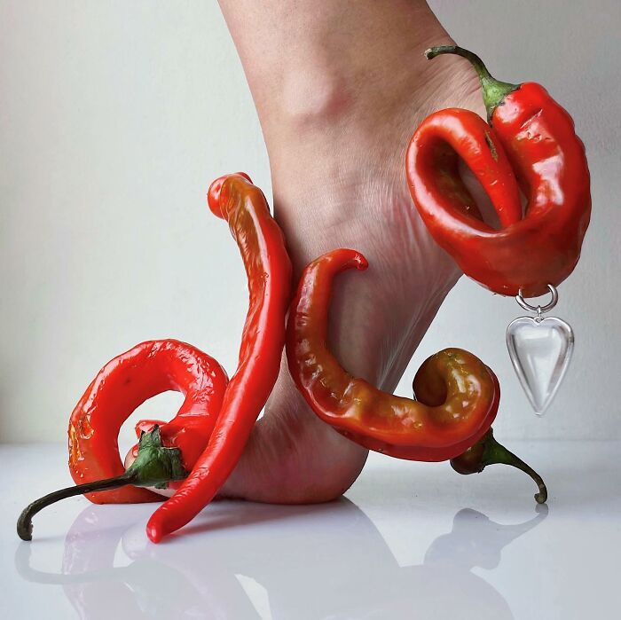 Foot adorned with sculptural footwear made of red chili peppers, showcasing creative artistry using everyday objects.