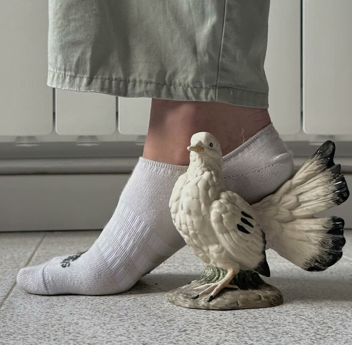 A ceramic bird used creatively as sculptural footwear on a foot wearing a white sock.