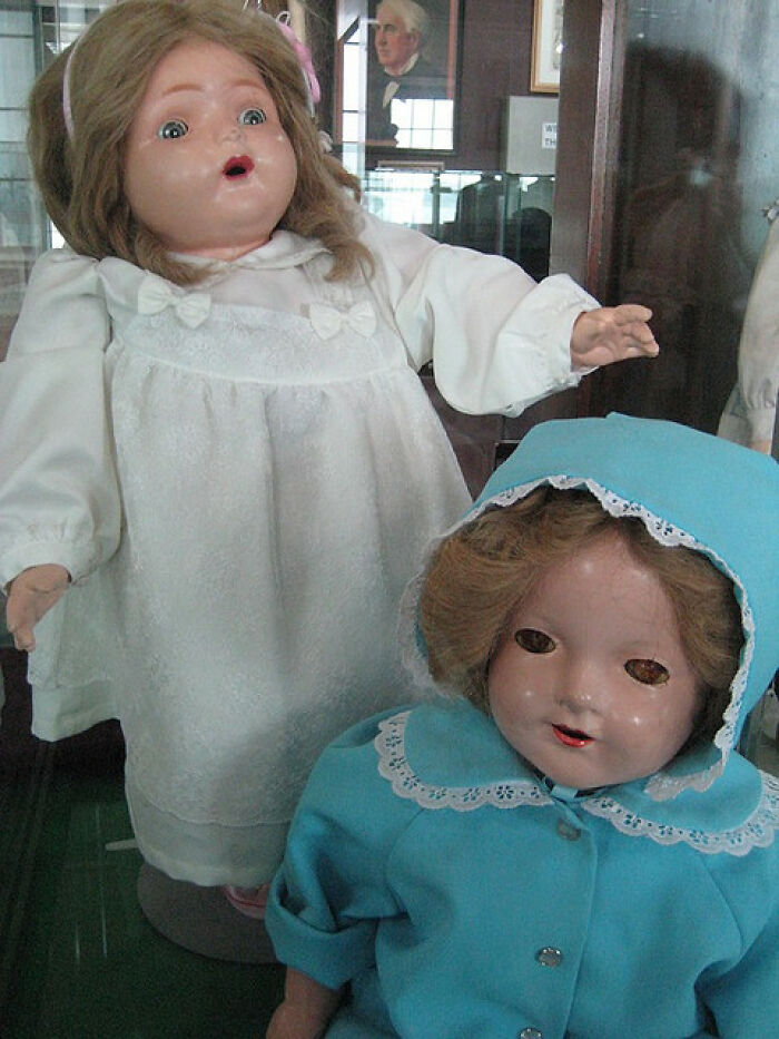 Two vintage dolls in a display case, showcasing historical inventions.