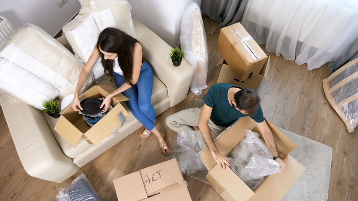 Couple unpacking boxes in a living room, surrounded by moving supplies and furniture.