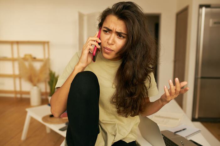 Woman on a phone call in a living room, looking concerned, representing tension with elderly in-laws.