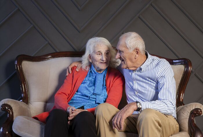 Elderly in-laws sitting on a sofa, engaged in a warm conversation, wearing casual clothes.