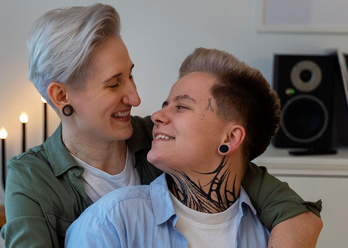 Two people with tattoos and short hair embracing, expressing self-love and confidence.