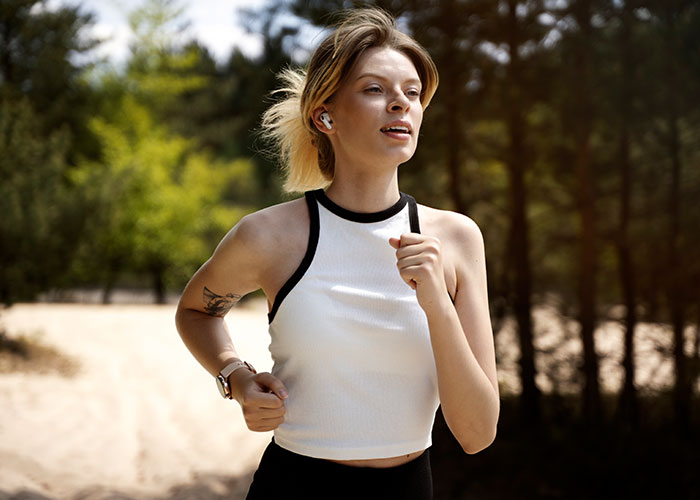 Woman confidently jogging through the forest, enjoying self-expression while wearing athletic gear and earbuds.