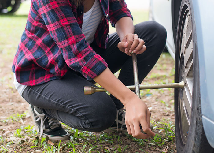 Woman confidently changing a car tire, showcasing independence and challenging societal norms.