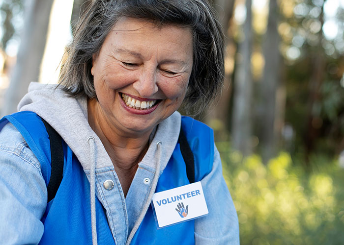 Smiling woman in blue vest with volunteer badge, embracing her uniqueness.