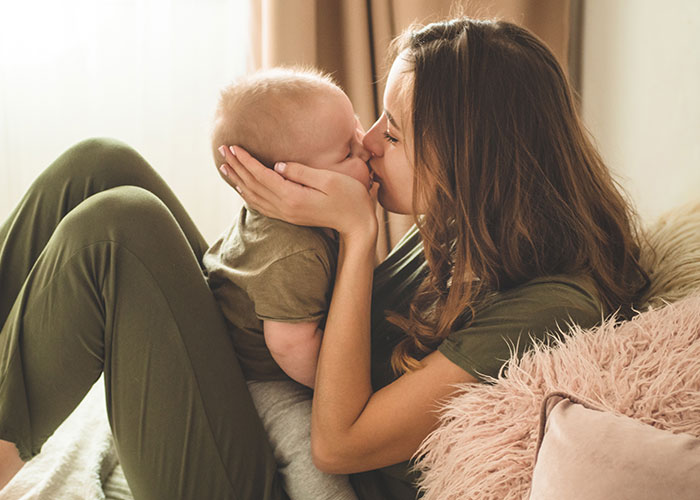 Woman lovingly holding baby on a cozy sofa, expressing joy and comfort.