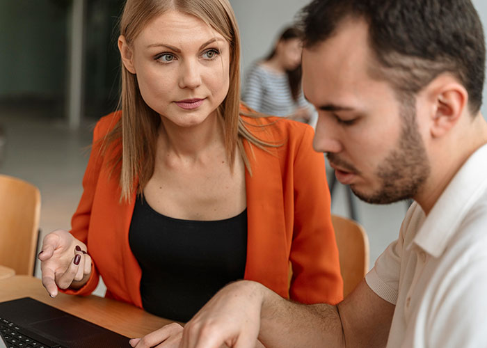 Woman confidently discussing work with a colleague, wearing an orange blazer, showcasing individuality.