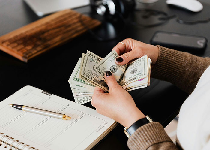 Woman counting money confidently at her desk, showcasing empowerment and self-assurance.