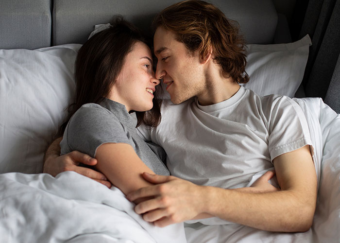 A couple lying in bed, smiling and embracing each other closely, expressing affection and happiness.