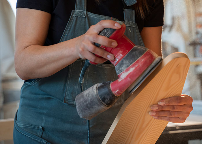 Woman confidently sanding wood with a power tool, embracing skills often seen as inappropriate for women by society.