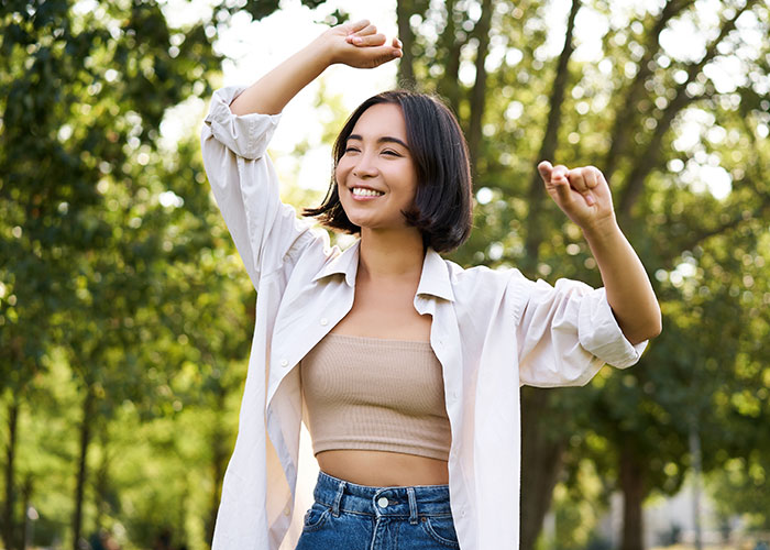 Woman joyfully dancing outdoors in casual attire, embracing personal confidence.