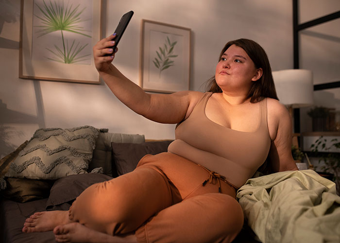 Woman confidently taking a selfie on a couch, embracing her uniqueness in a comfortable outfit.