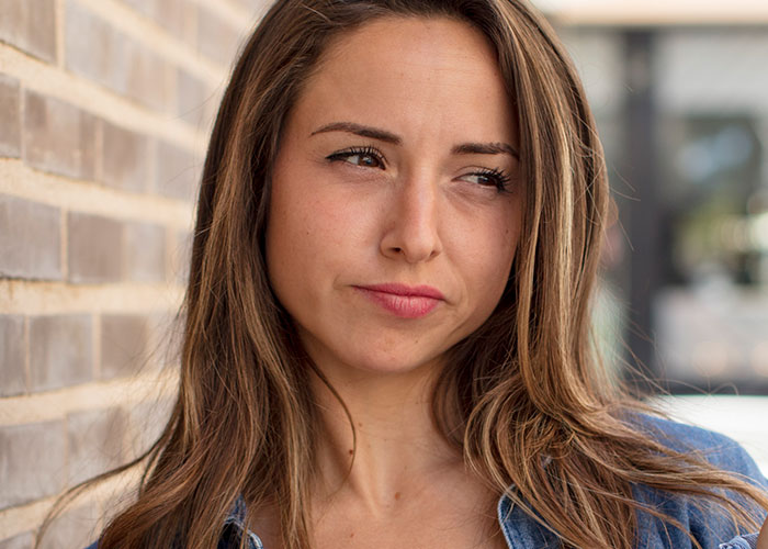 A thoughtful woman with long hair, standing against a brick wall, embracing her individuality.