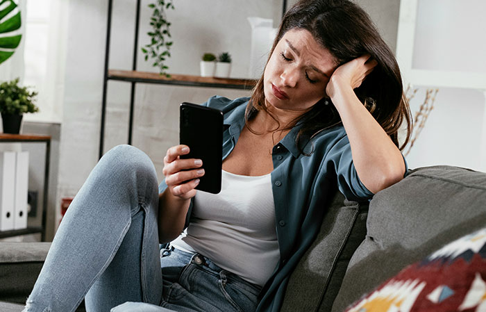 Woman looking frustrated on a couch while holding a phone, relating to unwillingness to babysit sister’s kids.