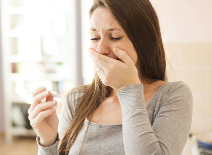 A woman in a gray top looks surprised while holding a test, conveying an emotional moment related to babysitting and motherhood.