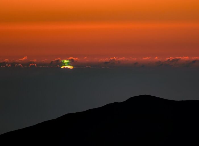 A stunning green flash at sunset viewed over a dark silhouette of a mountain, highlighting natural phenomena.