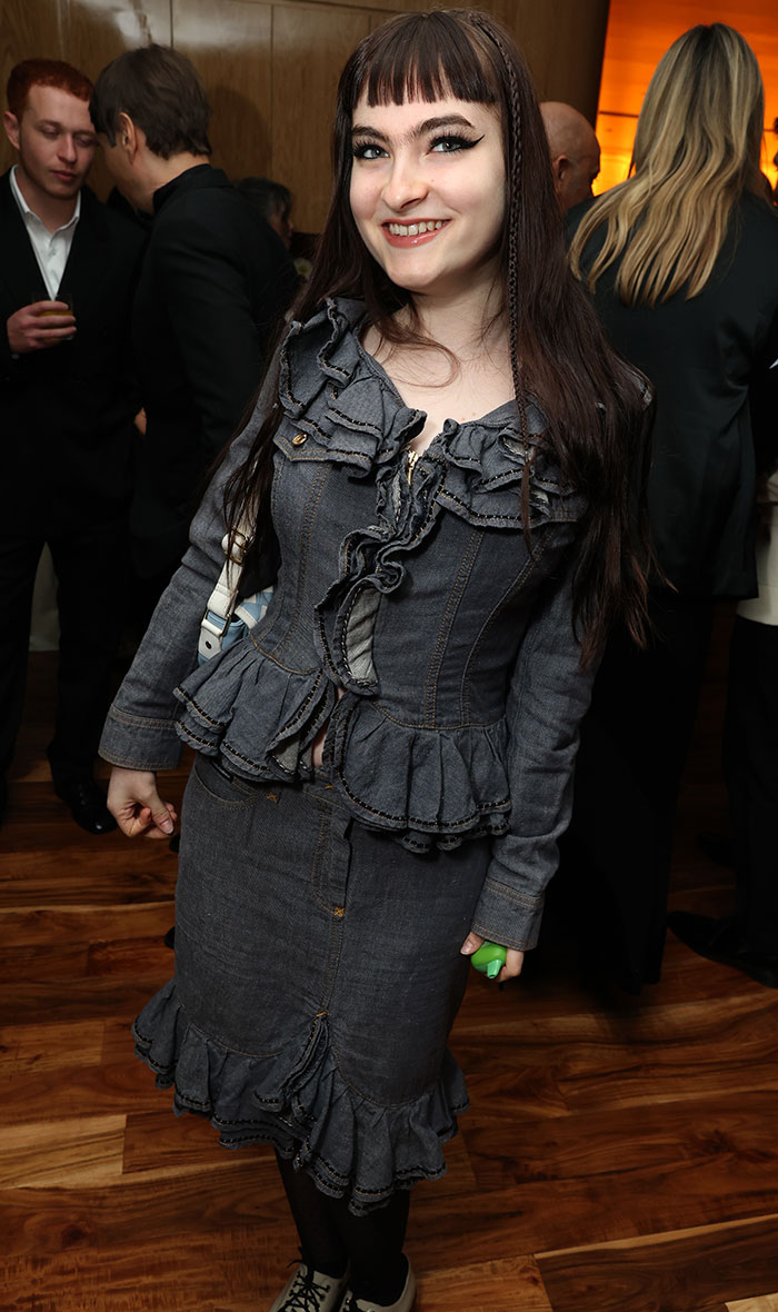 Ivy Wolk wearing a ruffled denim outfit at the Golden Globes 2025 after-party, standing on a wooden floor.