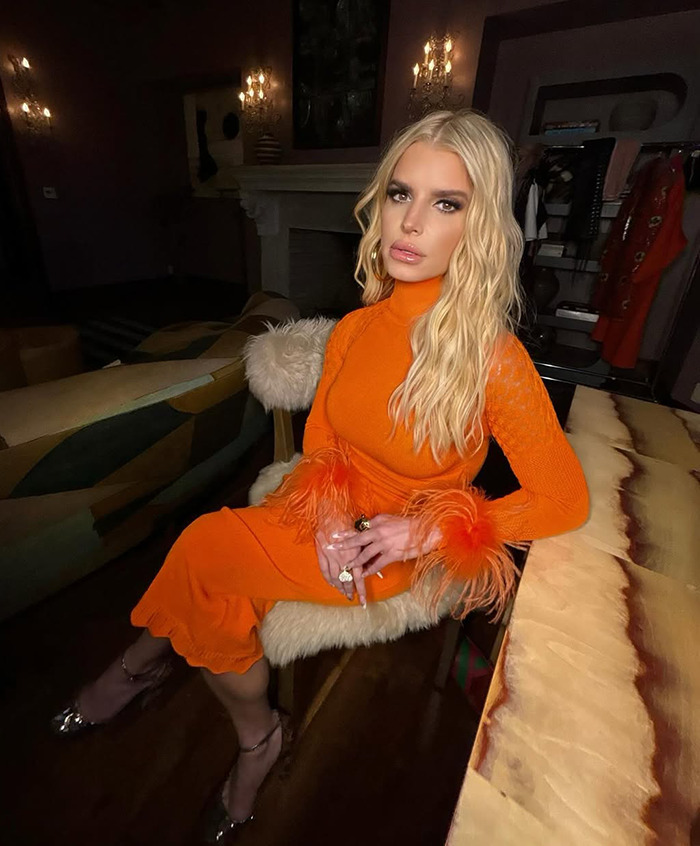 Blonde woman in an orange dress sits indoors, showcasing her "revenge body" confidently.