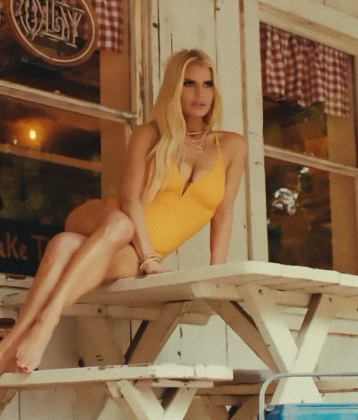 Blonde woman in yellow swimsuit sitting on a wooden table, showcasing revenge body outdoors.