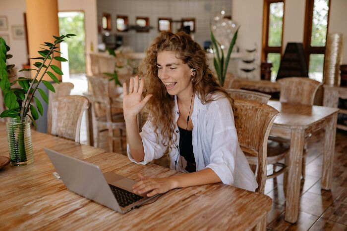 Person sitting at a wooden table, engaging in a video call on a laptop.