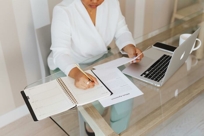 A person working at a desk with a laptop, notebook, and coffee cup.