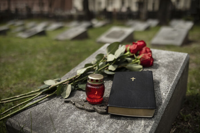 Red candle, Bible, and roses on a gravestone in a cemetery.