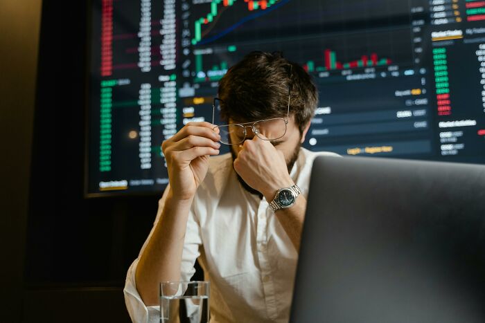 Stressed man working with stock market charts on a screen in the background.