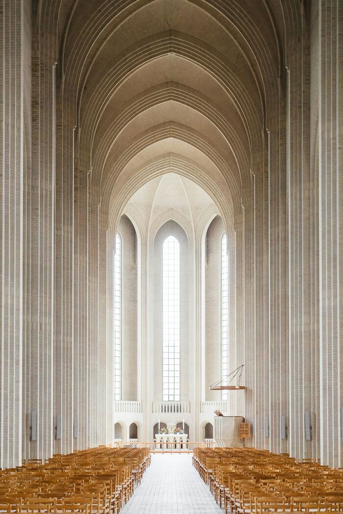 Interior view of a stunning church with high arches and rows of wooden chairs, creating a fascinating visual symmetry.