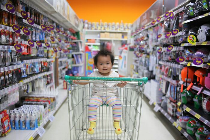 Baby sitting in a shopping cart in a store aisle, highlighting parenting choices.