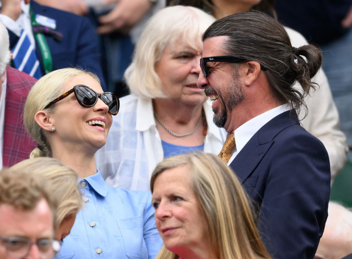 Jordyn Blum smiling in sunglasses with a man in a crowd, both engaged in conversation.