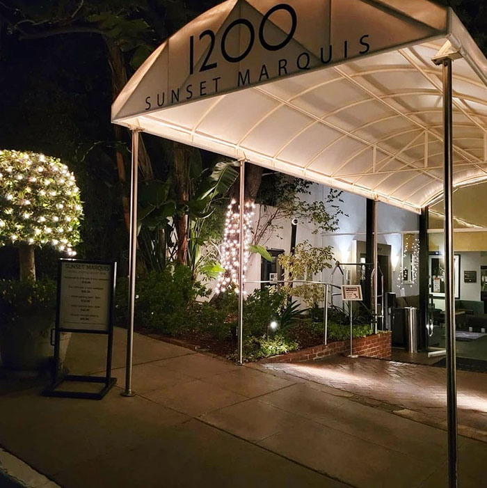 Exterior of 1200 Sunset Marquis lit at night, with greenery and festive lights.