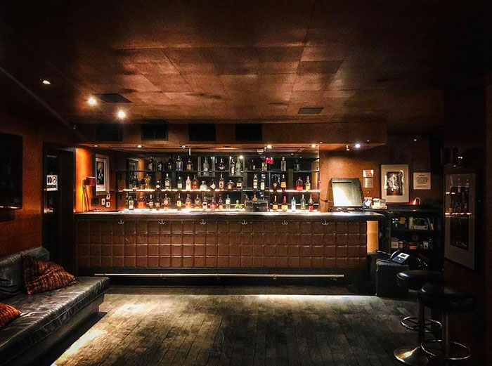 Dimly lit bar interior with stocked shelves and leather seating.