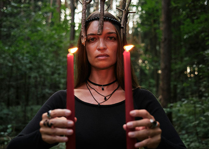 Woman in forest holding candles, representing strange human behavior.