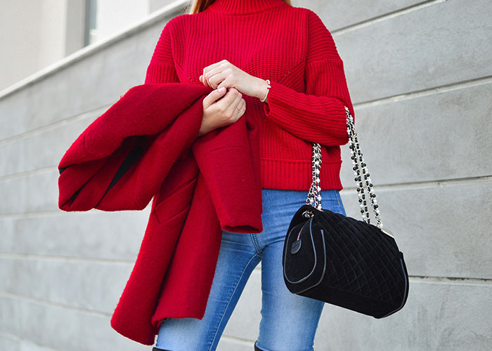 Person in red sweater holding coat, carrying a black handbag outside.