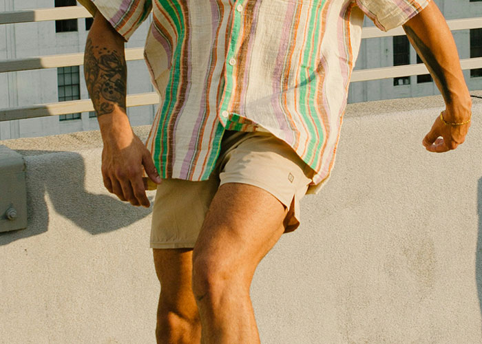 Man in striped shirt and shorts standing on rooftop, showcasing casual summer style.